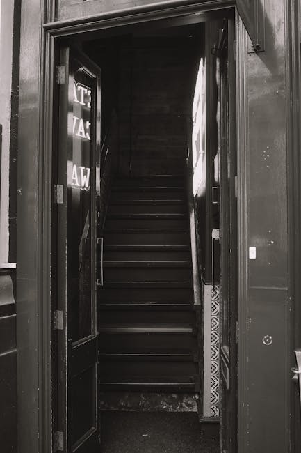 A set of internal industrial metal stairs with yellow safety handrails on either side, leading upwards within a warehouse or storage facility. The stairs have black and yellow anti-slip strips on each